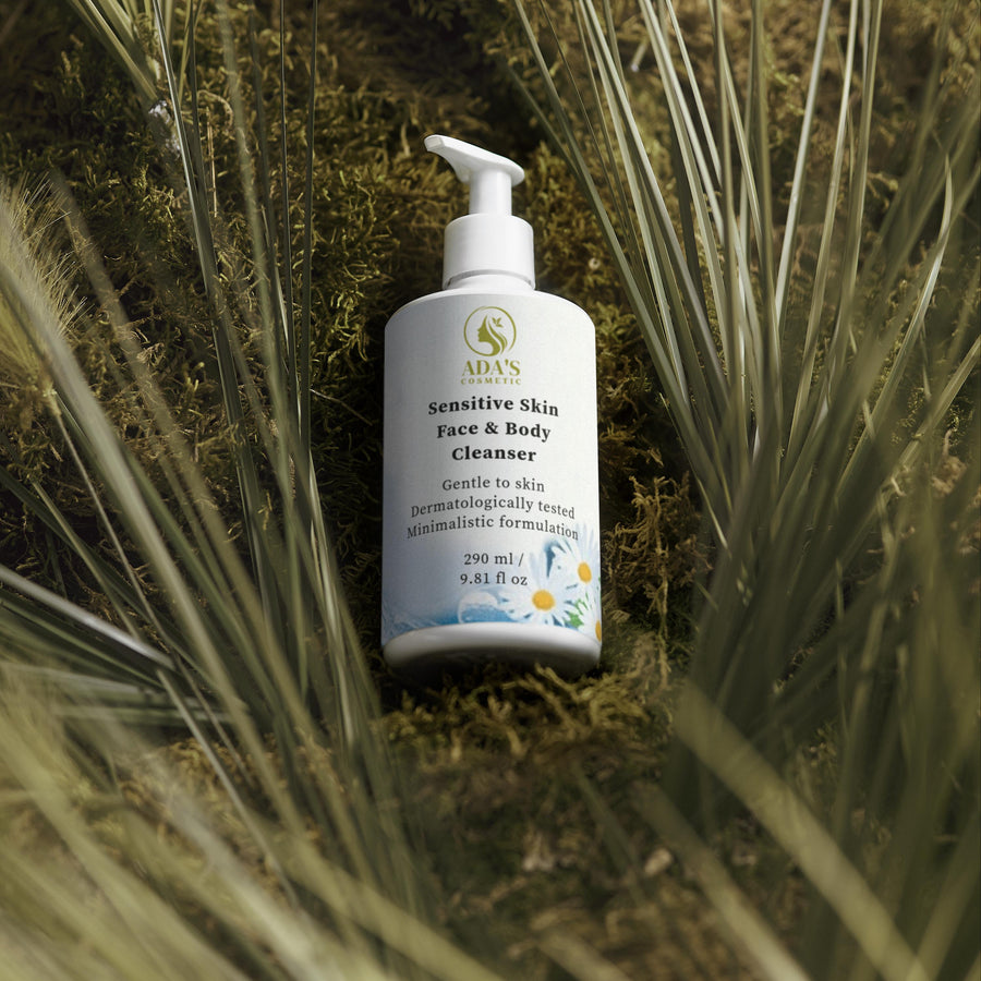 White bottle of sensitive skin face and body cleanser on a natural background with green plants.